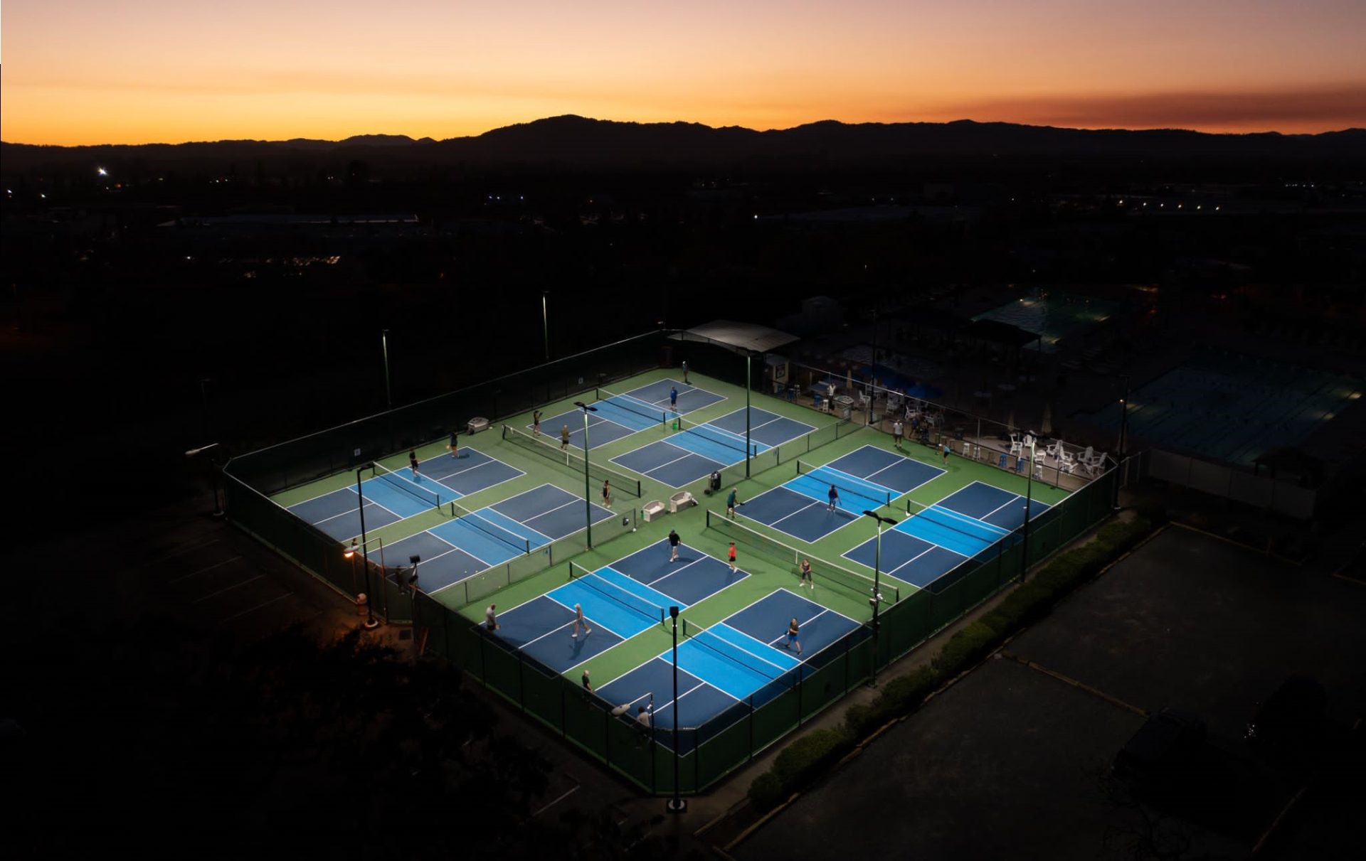 A drones photographs the Pickleball courts at Airport Health Club with a sunset.