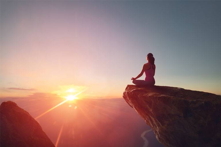 Woman sitting on a cliff and meditating during a sunset